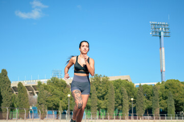 Woman with tattoos running on athletic track on a sunny day