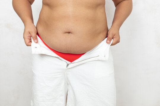 Unrecognizable overweight, obese woman with adipose belly try to put on too tight trousers on in white studio. Difficult buttoning and fast gaining weight. Abdomen after pregnancy, gain excess fat. 