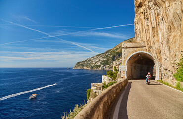Scooter drives along the road along the Amalfi coast, approaching the tunnel Conca dei Marini