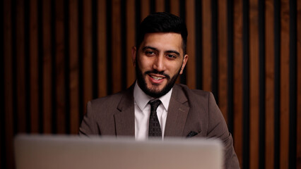 Handsome smiling latin man using laptop computer explaining something having video call.