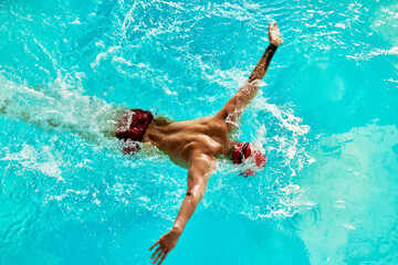 Swimming - male swimmer swimming breaststroke. Close up portrait of man doing breast stroke swimming in pool wearing red swimming cap and swim goggles