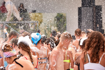 Foam party on the beach, bright sunny day crowd of people dancing on the foam, foam party,...