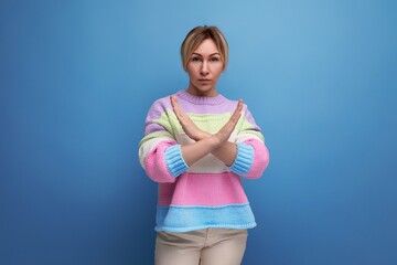 blond young woman in a striped sweater shows disagreement gesture of hands crossing them on a blue...