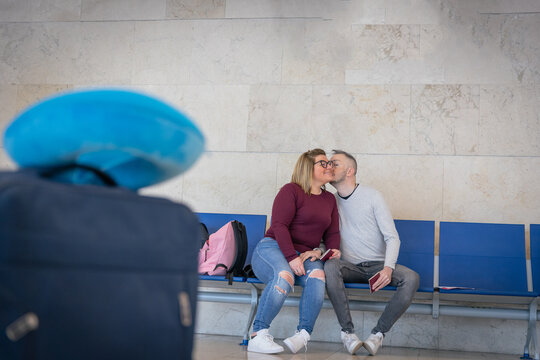 A Boyfriend Gives His Girlfriend A Kiss On The Cheek While They're At The Airport Waiting To Travel