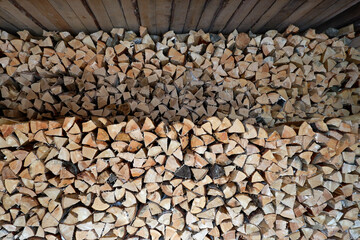 A pile of chopped wood stacked in two woodpiles under the roof. A lot of wood for a fire, burning in the oven.Buying and selling firewood for the winter. Storage and drying of firewood
