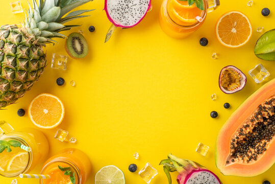 Bursting with tropical flavors. Top flat lay view photo of fresh fruit juice or cocktail in glass jar, dragon-fruit, kiwi, papaya, pineapple, orange, lime on yellow background with blank space