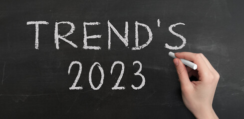 Fototapeta premium A woman's hand write text Trend's 2023 with chalk on chalkboard