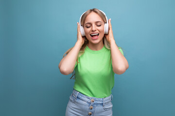 Obraz na płótnie Canvas adorable blond girl in casual outfit dancing to music in big white headphones on a blue background