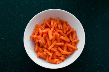 sliced ​​carrots in a plate on a dark background. juicy vegetables in a white bowl on a black board. healthy food concept