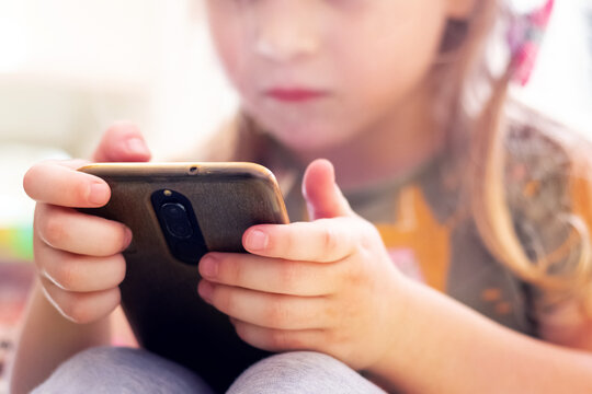 A little girl is looking intently at her phone. Children and modern technology. Phone dependency