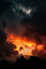 a flaming sunset with birds flying above trees, in the style of moody atmosphere, color splash, atmospheric clouds