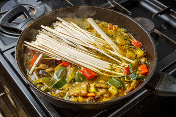 A frying pan with stewed vegetables in sauce and spices contains udon.