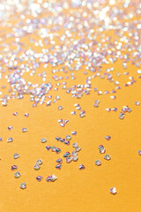 Shiny silver crystal confetti on a yellow background. Selective focus.