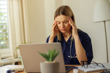 Tired female doctor using laptop while working at doctor's office. Healthcare concept