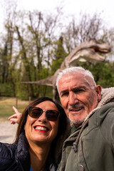 happy middle aged couple taking a selfie in front a dinosaur in a public park