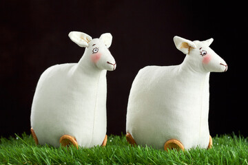 Two textile handmade sheeps (lamb) on the green grass at dark background