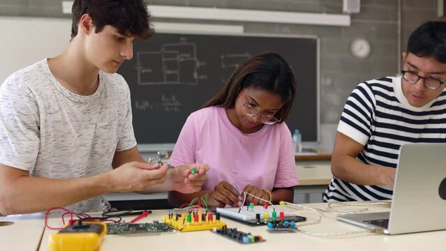 Group of diverse teenage high school students learning together to build electronic circuits at classroom. Millennial ethnic classmates working at technology class