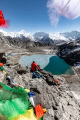 Papier Peint photo Makalu Hiker admiring views from Kongma-la pass with its lake below and Makalu,  Baruntse and Island peak in the background, photo framed with flying colorful prayer flags