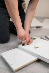 Furniture assembly. A worker is screwing a hinge into a wooden closet door. Adjustment of fittings, door hinges. The concept of installing furniture, home renovation.