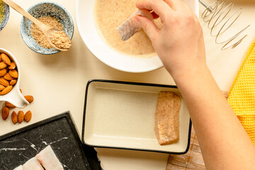making fish and chips, woman's hand making batter coated white fish for Britain, England, national traditional fried dish. Top view meal prep photo. 