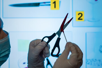 A crime lab technician holds scissors and takes a blood sample. In the crime lab. Against the background of a monitor with photographs of physical evidence.