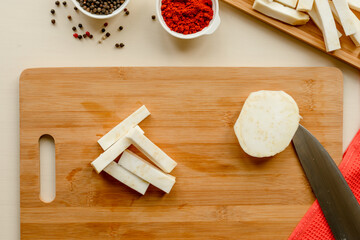 cutting board with raw celeriac and knife, top view photo celeriac for french fries along with black pepper and ground red pepper, cayenne