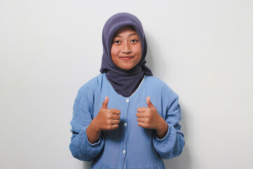 Cheerful young Asian girl in hijab showing two thumbs up