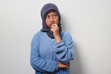 Pensive young Asian girl in hijab standing with fingers on chin