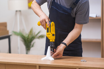 carpenter professional in coveralls uniform assemble furniture using yellow electrical drill and...