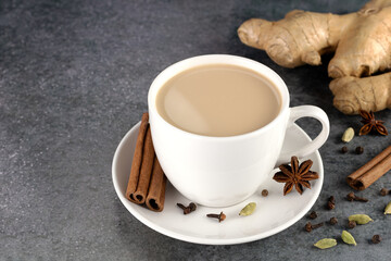 Indian masala tea in a white mug with spices - cinnamon, star anise, ginger, cloves, cardamom on a gray background.