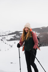 smiling girl on the mountain in winter with snowshoes on the backpack