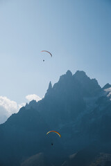 Two people doing paragliding sport in Chamonix next to Mont Blanc in the French Alps with blue sky and sharp rock spiers landscape in the background.