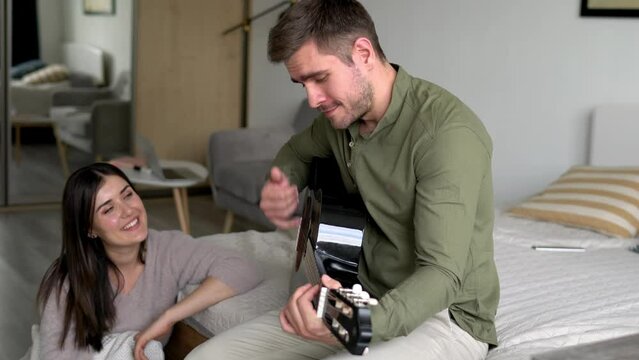 Untitled Project Clip 12Happy wife sitting at floor and listening positive music performance for inspired husband, Caucasian man with acoustic guitar playing sounds in home interior during weeknd fami