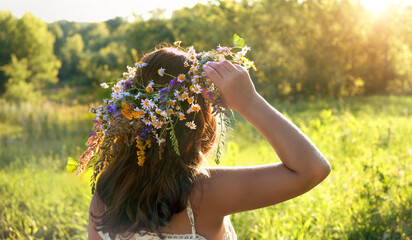 Girl in flower wreath on green sunny meadow, rear view. Floral crown, symbol of summer solstice. traditional Slavic ceremony for Midsummer, wiccan Litha sabbat. pagan folk holiday Ivan Kupala. - obrazy, fototapety, plakaty