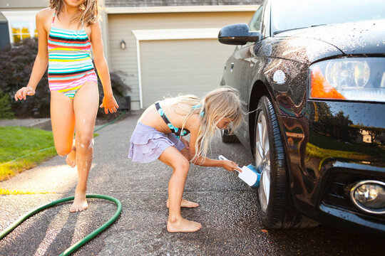Sisters washing car in the driveway of their home on a sunny summer afternoon in Portland, Oregon, USA