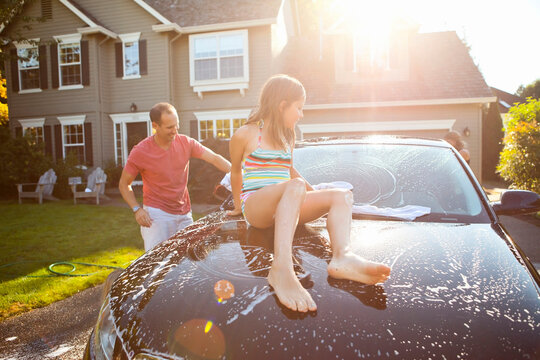 Family washing their car in the driveway of their home on a sunny summer afternoon in Portland, Oregon, USA