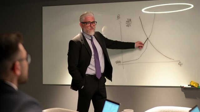 Caucasian male mentor explaining business marketing information during cooperation meeting with colleagues in board room, coacher in suit training employees during brainstorming briefing
