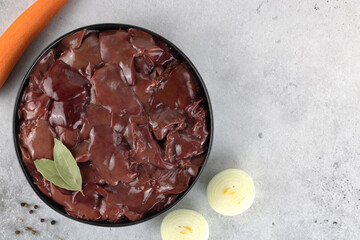 Raw chicken liver on a black plate with carrots, onions and spice on a gray background. Noise to tail concept.
