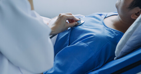 Side view of diverse doctors examining Asian female patient in bed in ward at hospital.