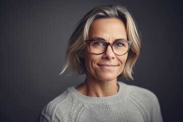 Portrait of a beautiful middle-aged woman wearing glasses and a sweater on a gray background