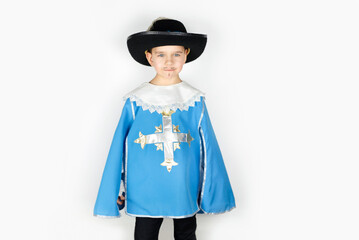 A happy young boy on a white background in a blue musketeer fancy dress costume with a black cape, the boy imagines himself to be strong and brave