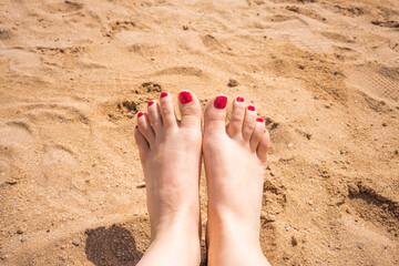 Female feet with manicured nails on the beach sand.