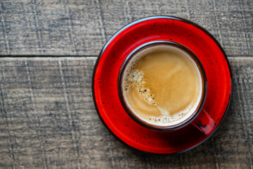 Red porcelain coffee cup with saucer over wooden background, top view, copy space, closeup. Hot coffee in a breakfast