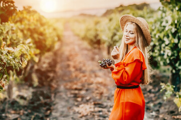 Portrait of a happy woman in summer vineyards at sunset. a woman in a hat and a red dress holds...