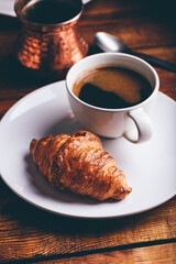 Cup of Black Coffee and Fresh Croissant on Wooden Table