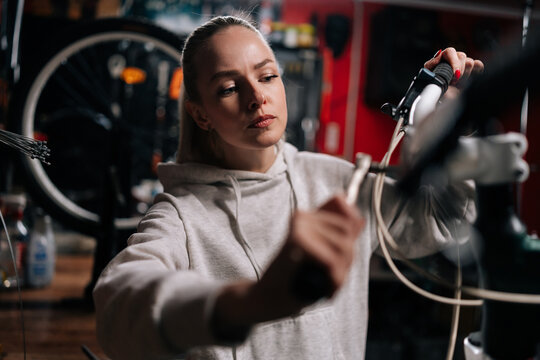 Closeup of serious blonde cycling mechanic female fixing bicycle handlebar with special tools working in bike repair shop with dark interior. Concept of professional maintenance of bicycle transport.