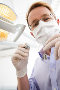 Dentist wearing Surgical Mask and Holding Dental Instruments looking down, Germany