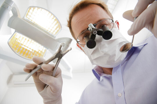Dentist wearing Surgical Mask and Magnifier looking down, Germany