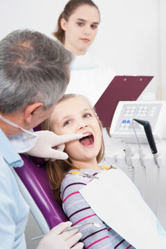 Dentist touching Girl's tooth and Hygienist with Clipboard during Appointment, Germany