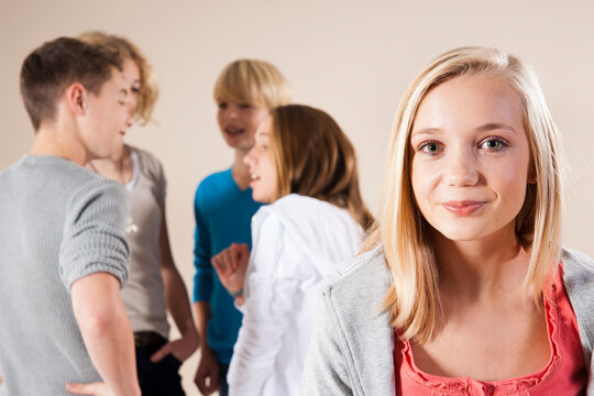 Portrait of Blond, Teenage Girl Smiling at Camera with Group of Teenage Boys and Girls Talking in Background, Studio Shot on White Background